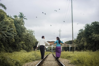 woman and man holding hands while walking on train tracks