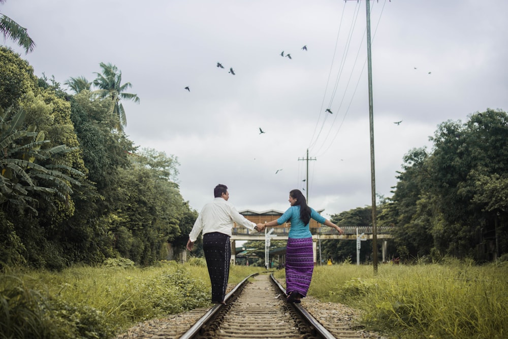 woman and man holding hands while walking on train tracks