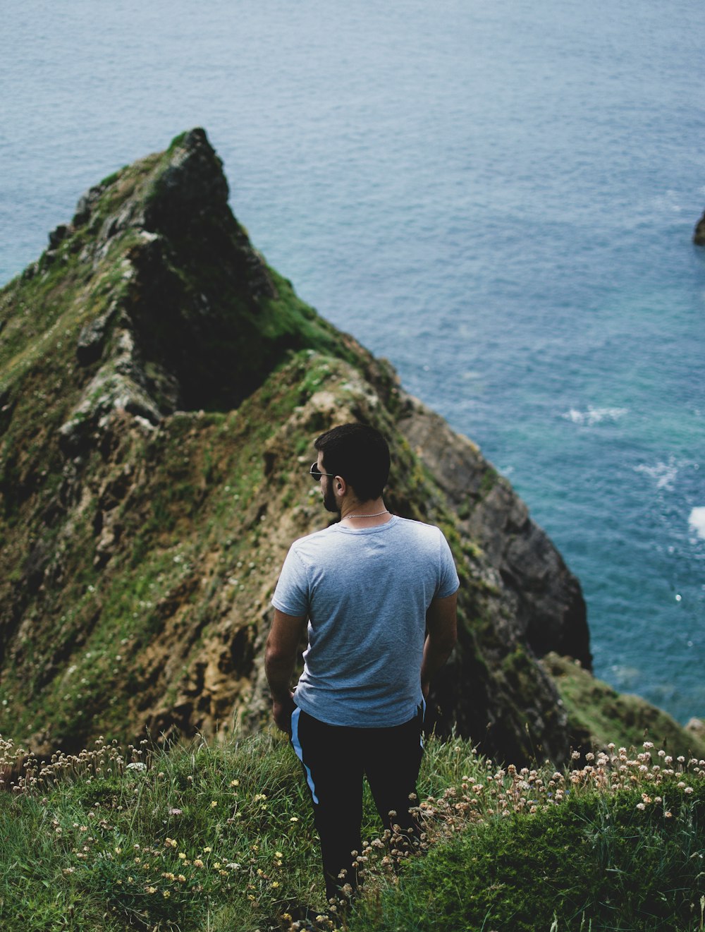 man standing near cliff while facing body of water at daytime