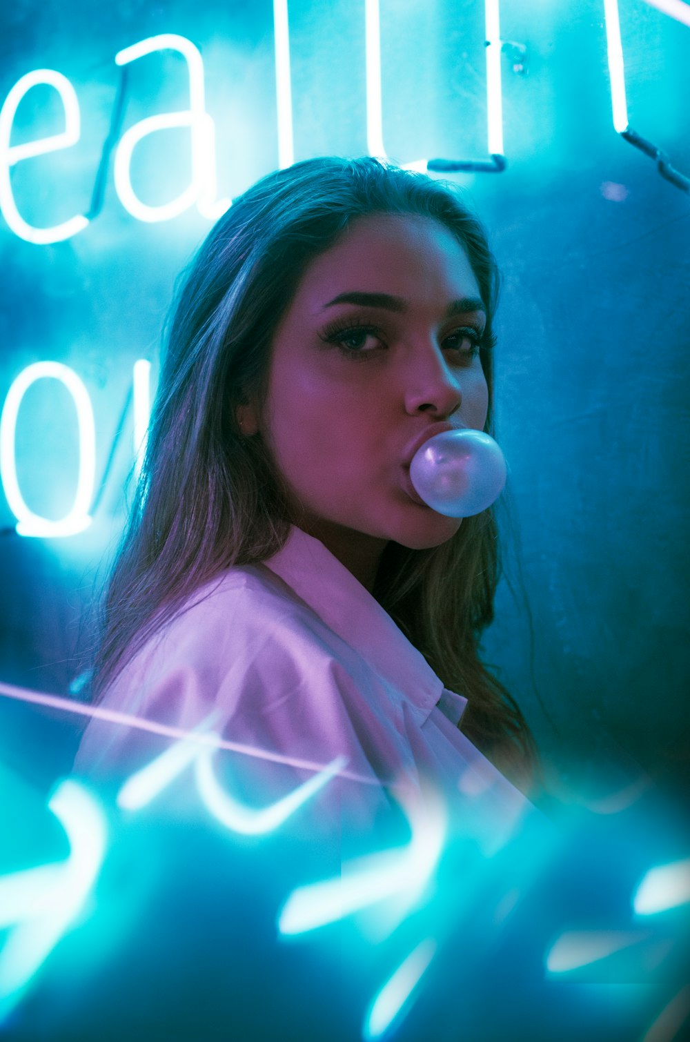 selective focus photo of woman blowing gum standing in front of turned-on neon signage