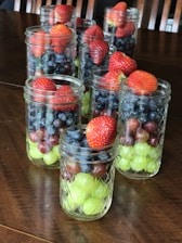A close-up of fresh fruits and jars of natural fruit jam arranged neatly on a wooden table.