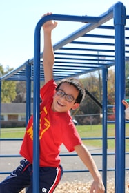 A child confidently crossing monkey bars with a big smile on a bright day.