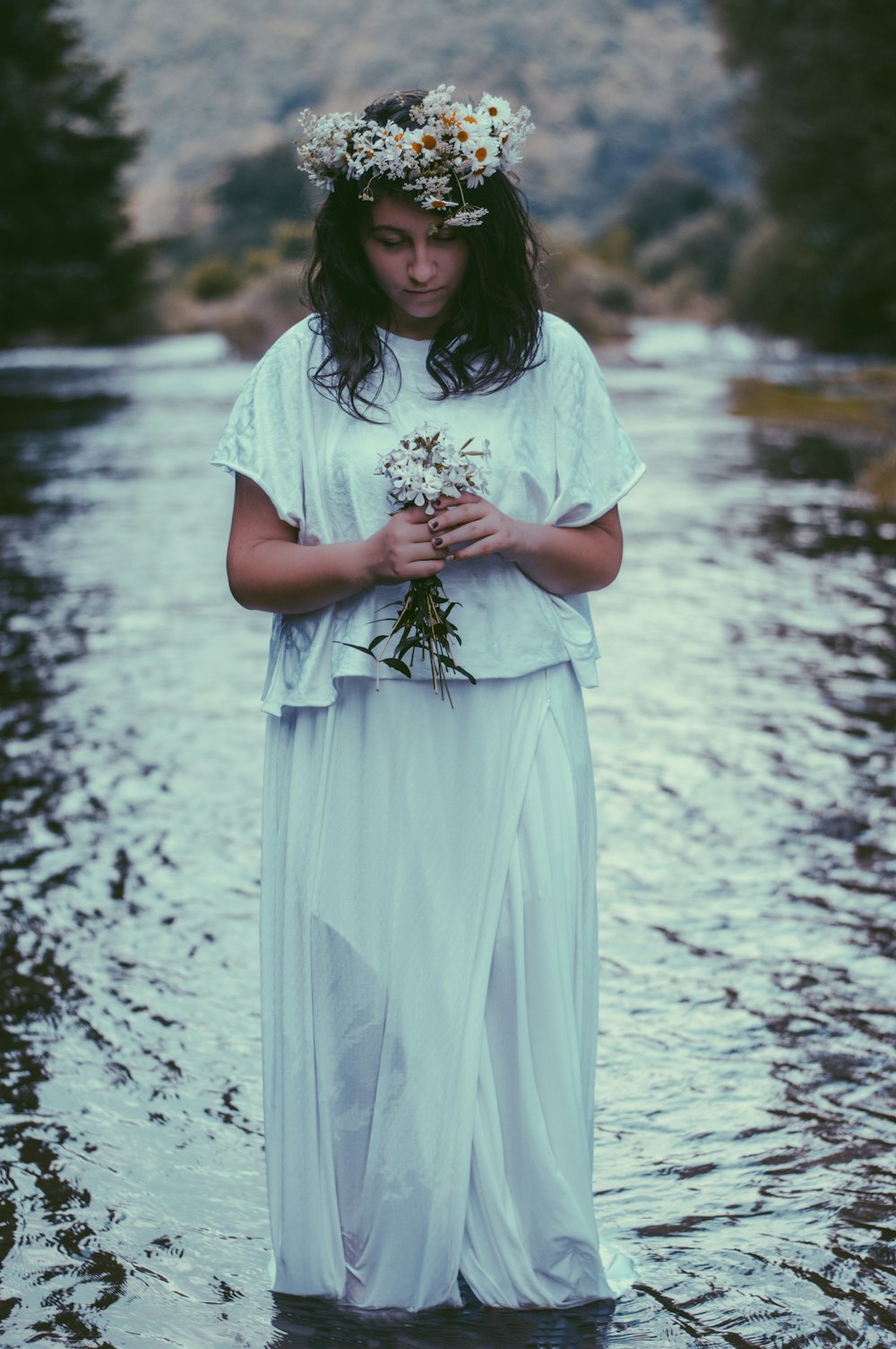 donna che indossa il vestito e tiene il fiore in piedi nello specchio d'acqua