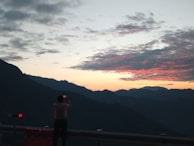 A traveler photographing a breathtaking sunset over distant mountains.