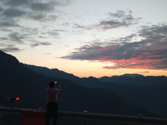 A traveler photographing a breathtaking sunset over distant mountains.