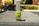 A tennis ball branded with 'Wilson Hope' is centered in focus on a blurred background that appears to be outdoors. There is a faintly visible object in the foreground, possibly a lens cap or a similar small item. The background is out of focus, with traces of greenery and what looks like a can or container.