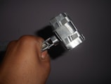 A hand holding a homemade hammer-like object made of metallic components, featuring a blocky head and handle secured with metal strips.