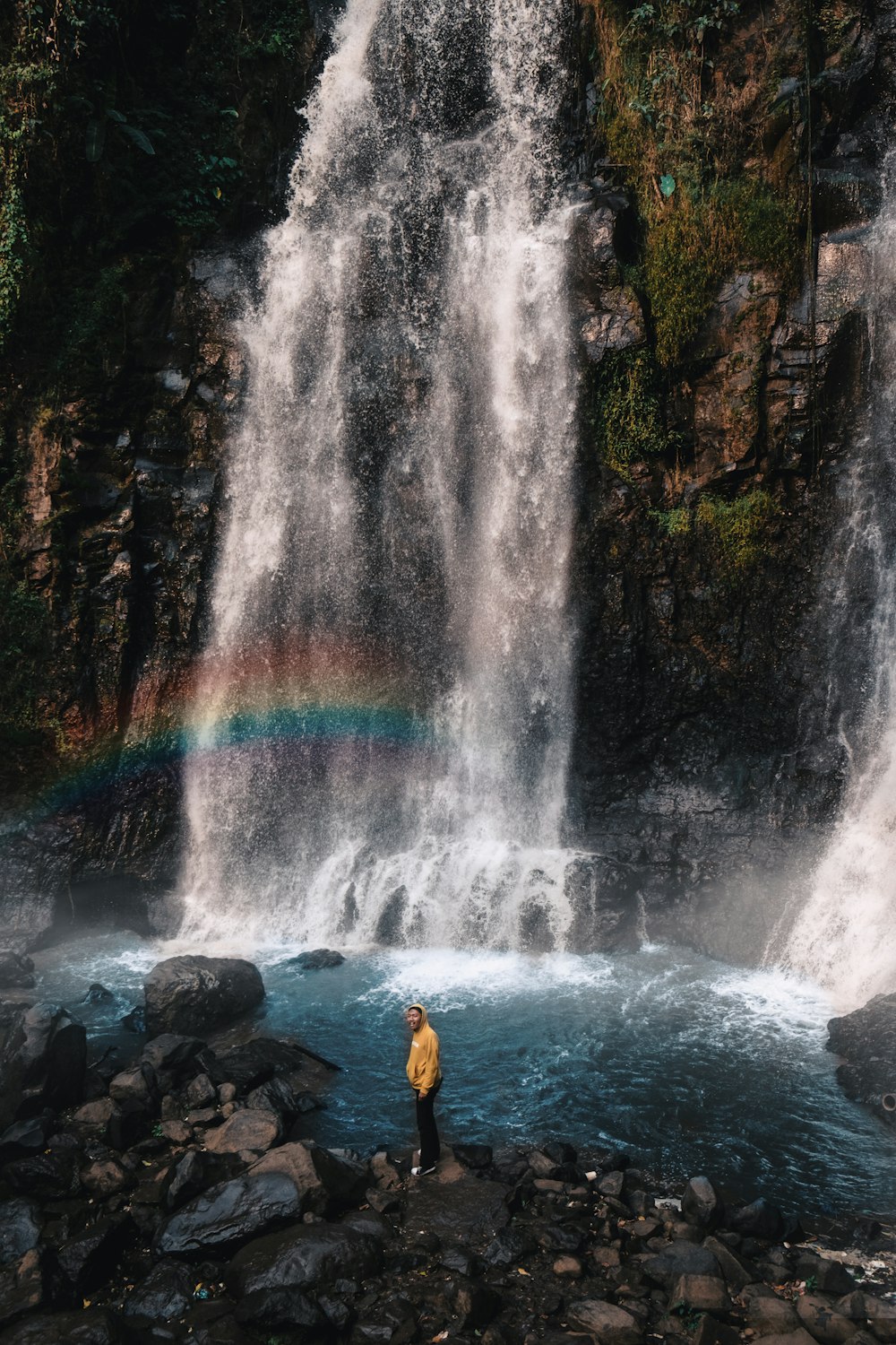 man standing on rock near waterfalls