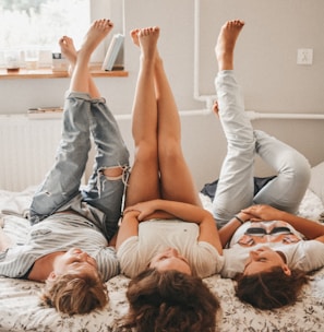 three women lying on bed while raising their feet