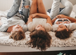 three women lying on bed while raising their feet