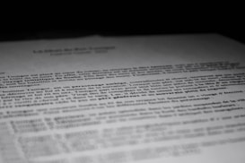 A close-up of a printed document with text in French, partially blurred, with the focus on specific lines of the text. The contrast between the dark background and the white paper emphasizes the content.