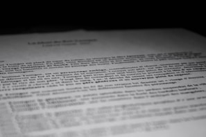 A close-up of a printed document with text in French, partially blurred, with the focus on specific lines of the text. The contrast between the dark background and the white paper emphasizes the content.