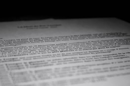 A close-up of a printed document with text in French, partially blurred, with the focus on specific lines of the text. The contrast between the dark background and the white paper emphasizes the content.