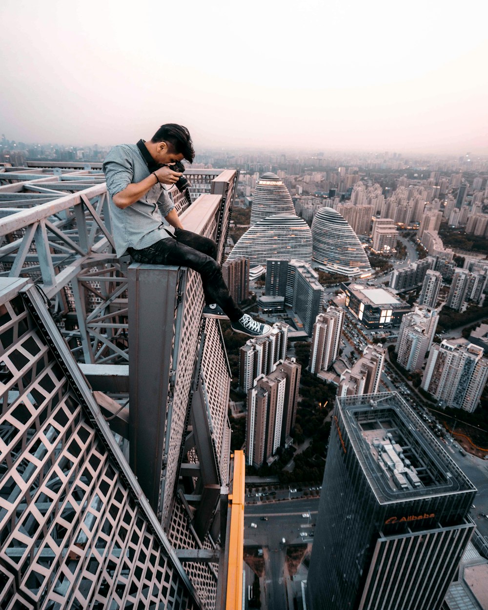 homem sentado em cima do prédio tirando foto abaixo