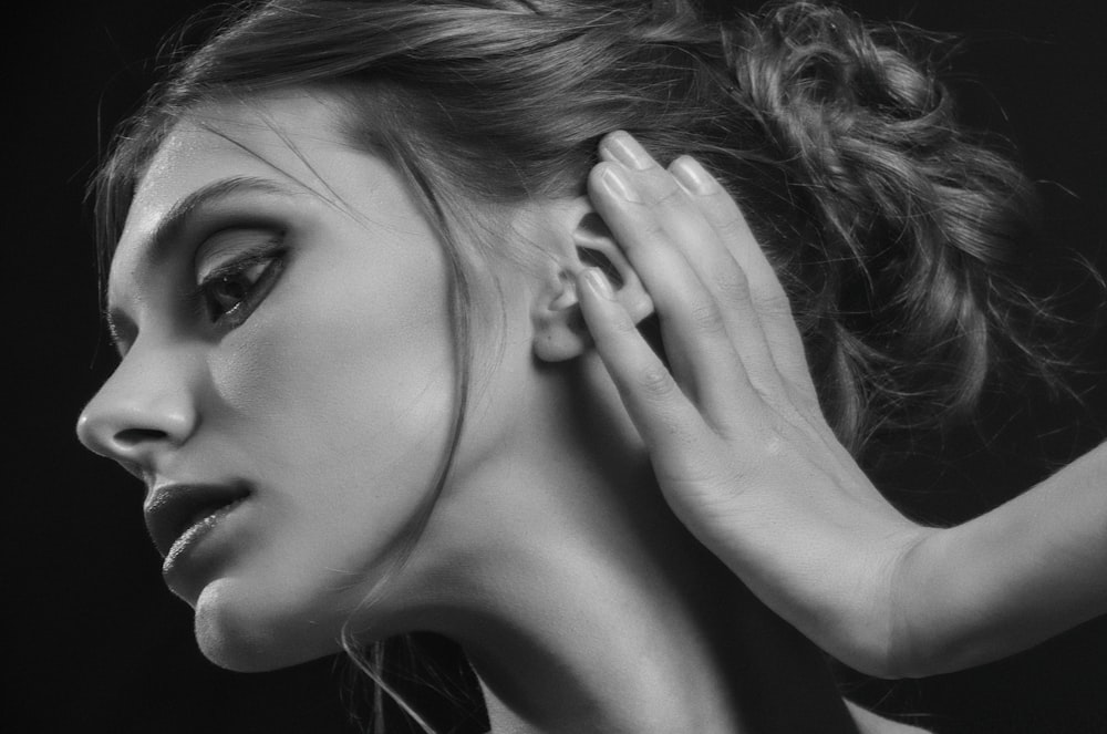 grayscale photography of woman holding hear ear