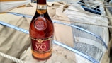A bottle of brandy with a maroon and gold label is placed on a tan paper surface. The bottle is surrounded by packaging material including bubble wrap and ropes.