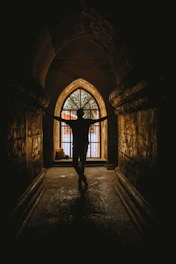 A shadowy figure entering a dimly lit underground doorway bathed in red light.