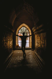 A shadowy figure entering a dimly lit underground doorway bathed in red light.