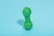A green rubber dog toy with a bumpy texture is placed upright on a light blue background. It casts a subtle shadow to its left, suggesting a light source from the right.