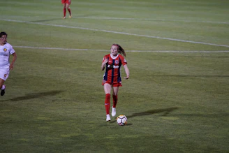 Young female soccer player skillfully dribbling the ball on a sunny field.