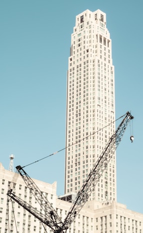 A wide shot of a commercial building rising with cranes against a clear blue sky.