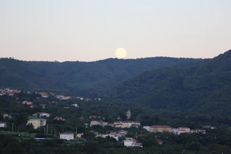 Delicate watercolor of a sleepy moon watching over a cozy village at night.