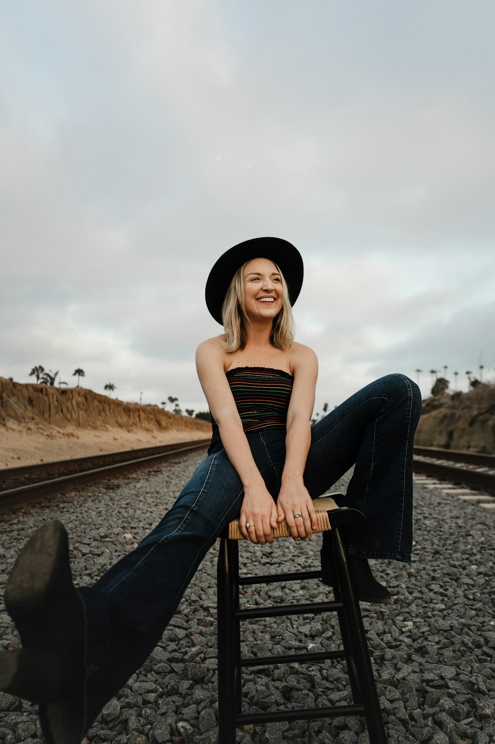 woman sitting on stool in the middle of train rails during cloudy day