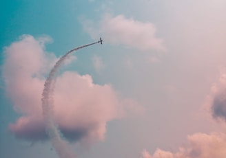 low angle photography of plane flying at high altitude with track of smoke during daytime