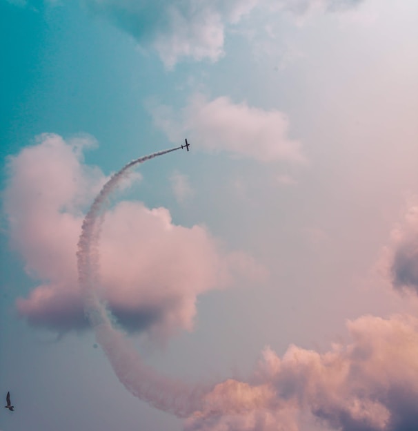 low angle photography of plane flying at high altitude with track of smoke during daytime