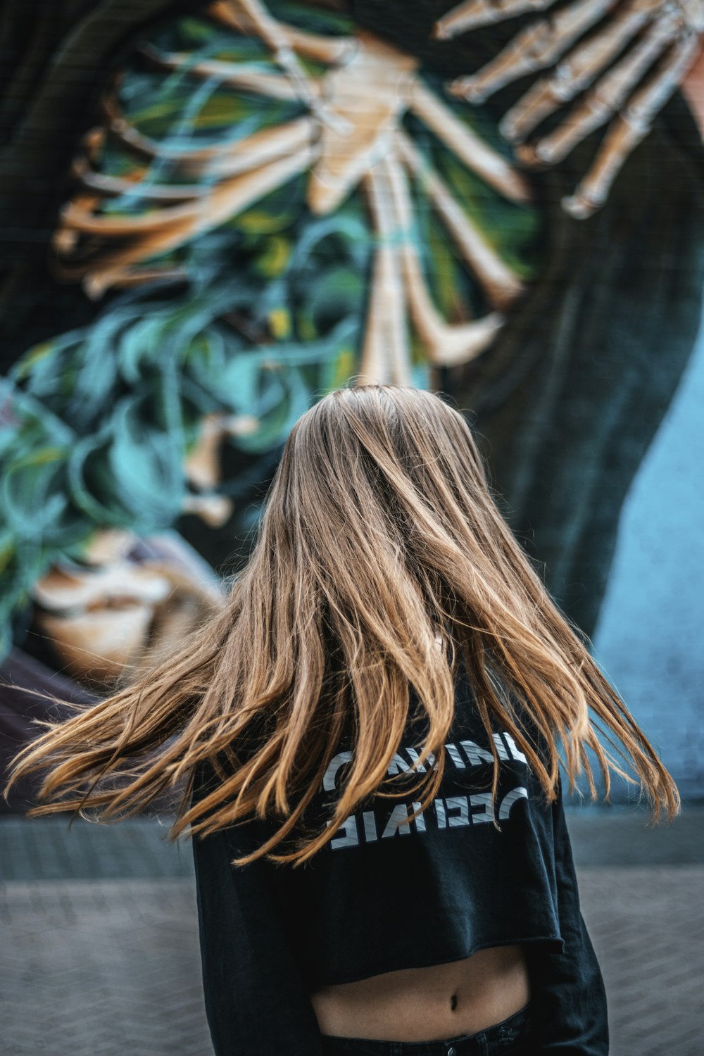 brown haired woman wearing black crop-top sweatshirt making a hair spin near green wall