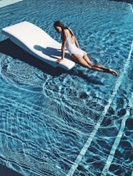 woman lying on white lounge chair in the middle of pool