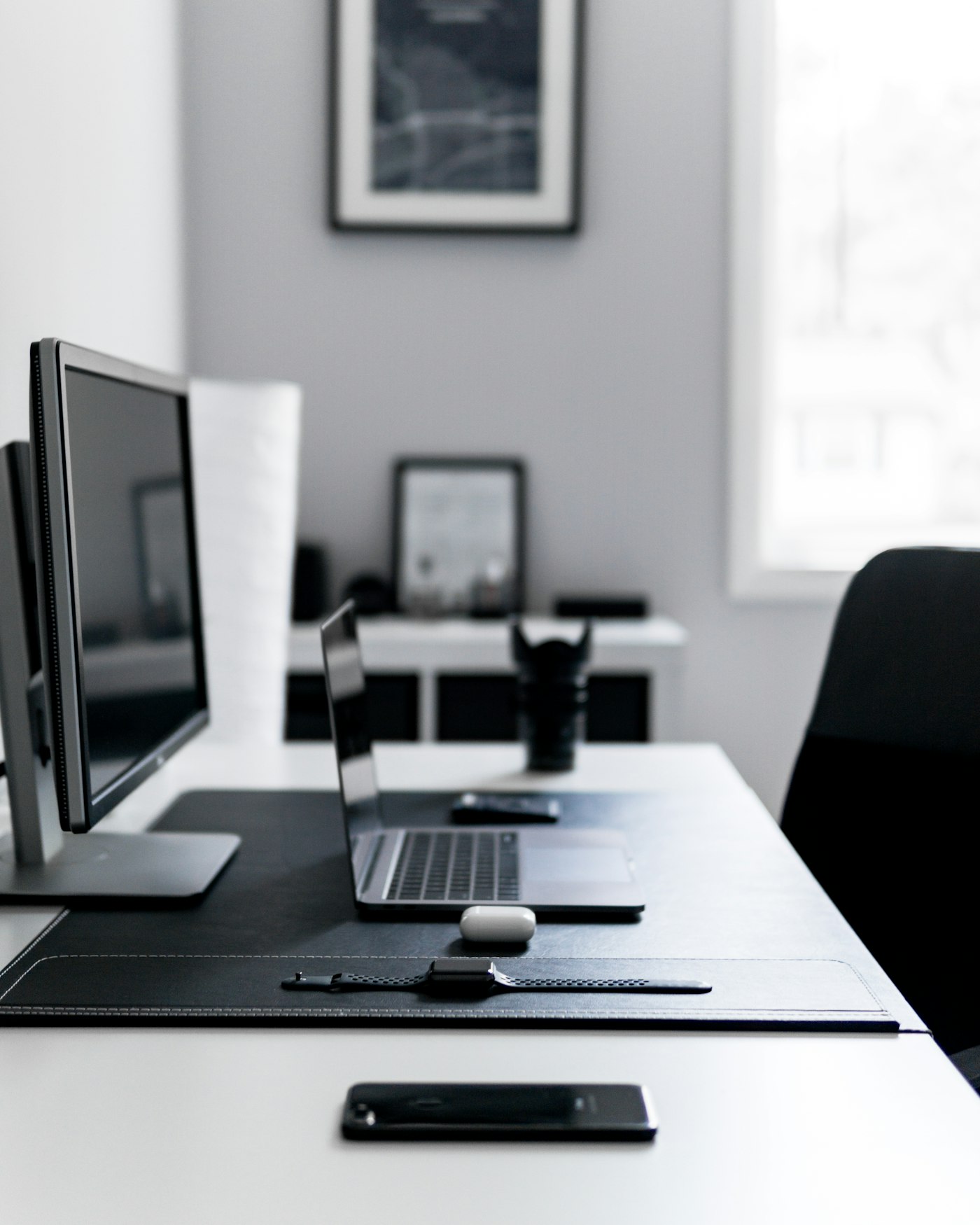 Open laptop and external monitor on a white desk beside a phone, smartwatch and earbud case.