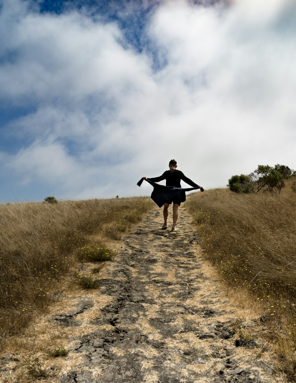 Mujer sosteniendo chaqueta caminando en camino de tierra durante el día