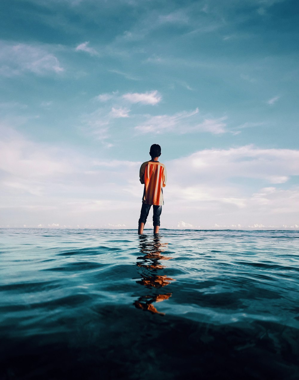 person wears orange top standing on sea during daytime