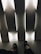 The image presents a pair of black shoes worn by an individual seated indoors. The setting includes vertical, white, illuminated panels casting a soft, ambient light across the floor. The overall feel is minimalistic and modern, with strong angular lines and contrasting light and shadow.