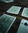 Several playing cards are scattered across a rustic wooden surface. The cards have intricate green designs on their backs, with one card facing up displaying the number five of spades.