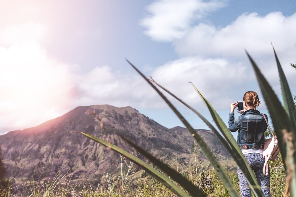 woman wearing blue denim jacket while taking photo of brown mountain