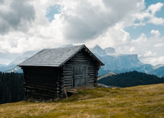 wooden house on grass field on hill under cloudy sky at daytime