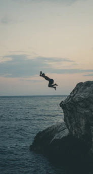 A fearless adventurer mid-air, soaring over jagged cliffs during a daring base jump at sunset.