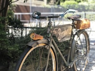 A vintage bicycle leaning against a wrought-iron fence, draped with a light scarf and a basket of fresh bread.