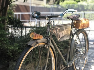 A vintage bicycle leaning against a wrought-iron fence, draped with a light scarf and a basket of fresh bread.