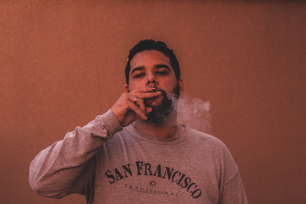 man wearing gray San Francisco long-sleeved shirt while smoking