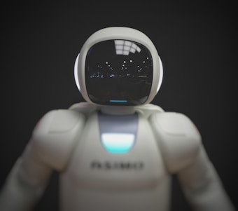 A humanoid robot with a smooth, white exterior and a glossy, reflective helmet-like faceplate. The robot appears to have glowing sensors or lights.
