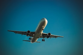An airplane is captured mid-flight against a clear, blue sky. The aircraft appears to be in a landing or takeoff phase, with its landing gear visible. The angle of the shot emphasizes the wingspan and engines.