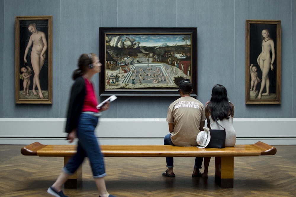 man and woman sitting on bench while looking at painting