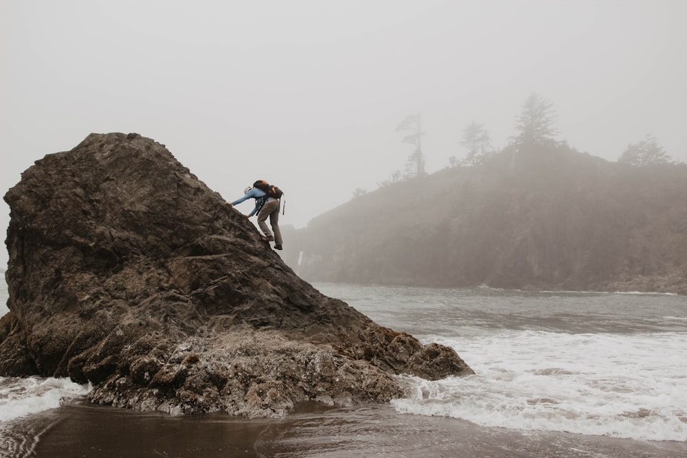 man climbing rock formation by water