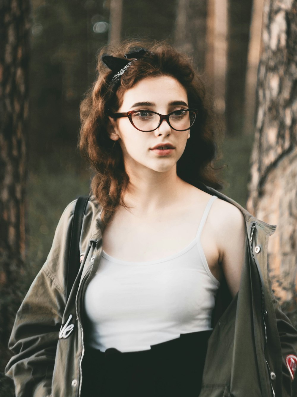 woman wearing white camisole and gray jacket standing near tree selective focus photography