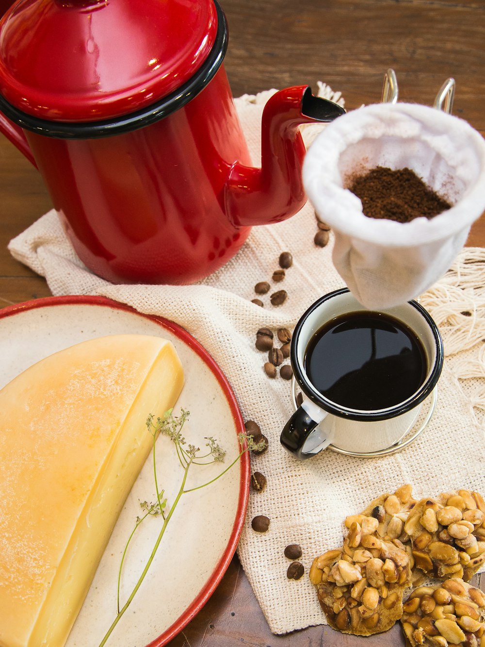 chaleira vermelha e preta perto de caneca cheia de café e meio queijo na mesa