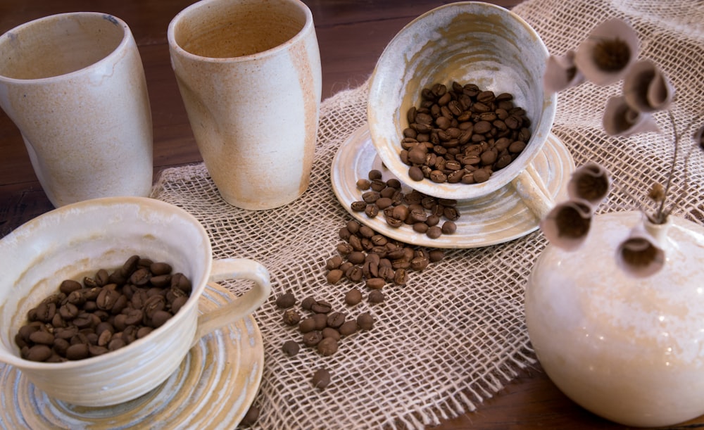 coffee beans spilled on saucer plate and table cloth near white ceramic vases