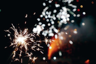 A vibrant and energetic display of bright sparks, with small firework explosions spreading in different directions against a dark background. The warm, glowing lights create a shimmering effect.
